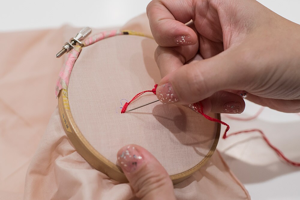 2 刺繍糸の束から3本取り分け、針に糸を通して糸の端を玉結びする。ぷっくりとした立体的なハートにするために、布の裏から針を入れ、中央から下にかけて４本、横に向かって針を刺すサテンステッチをする。
